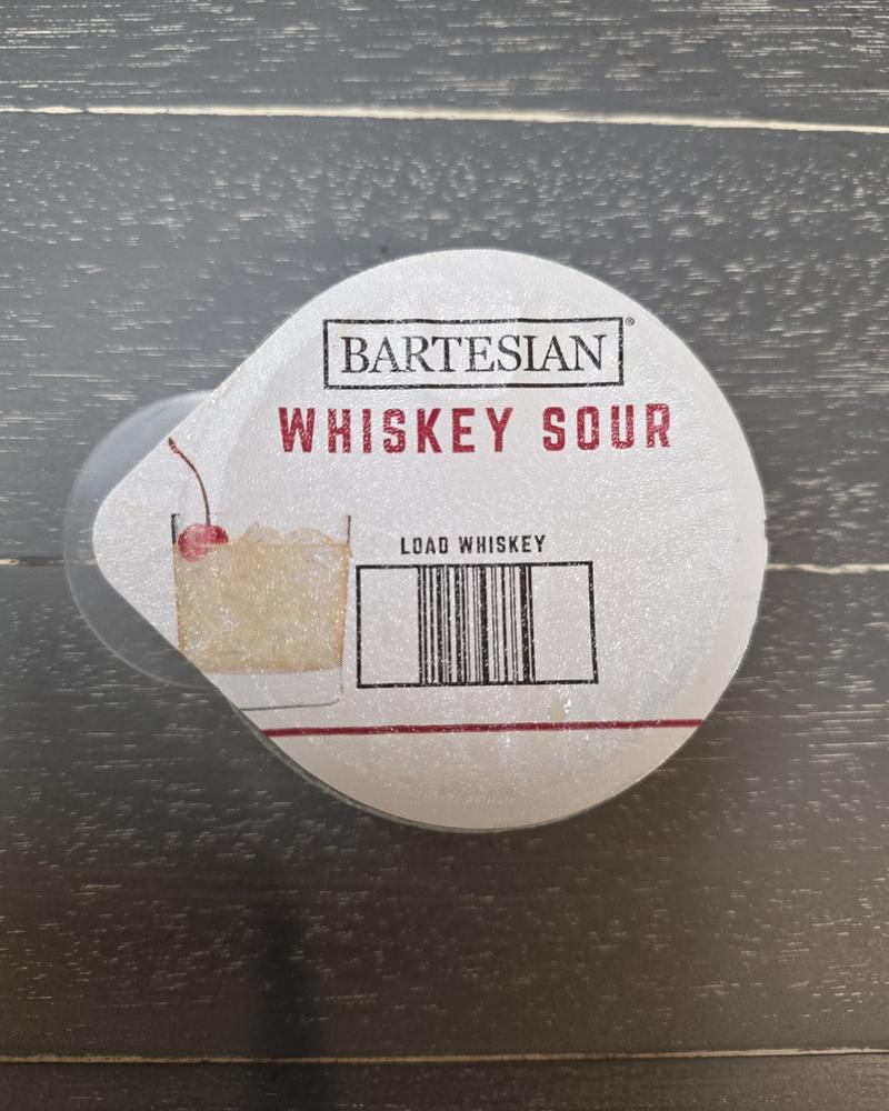 Top-down close-up of a Bartesian Whiskey Sour pod lid showing the printed barcode and the Load Whiskey label