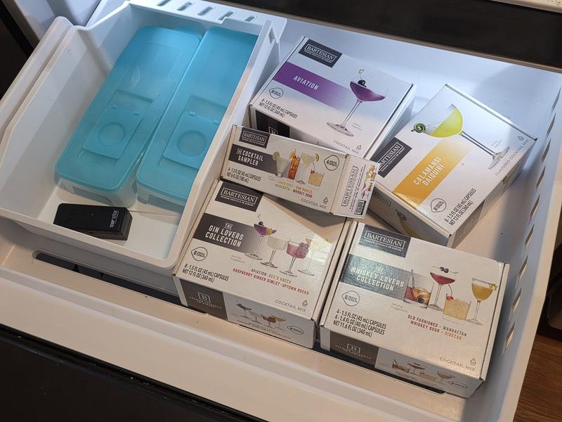 Boxes of Bartesian pods, including Aviation, Calamansi Daiquiri, the Cocktail Sampler and the Gin Lovers and Whiskey Lovers Collections, stored in a drawer beside blue ice packs