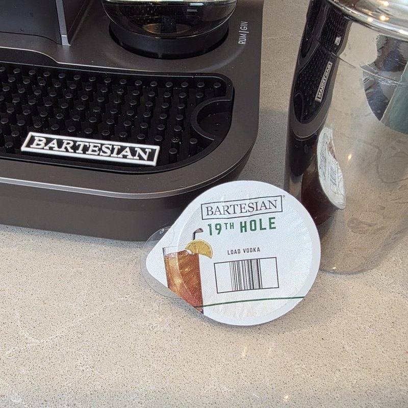 The Bartesian 19th Hole capsule resting on the counter beside the machine, label and Load Vodka instruction clearly visible
