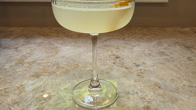 Bartesian Bee's Knees cocktail in a coupe glass with a pale yellow color and a lemon garnish on a home bar