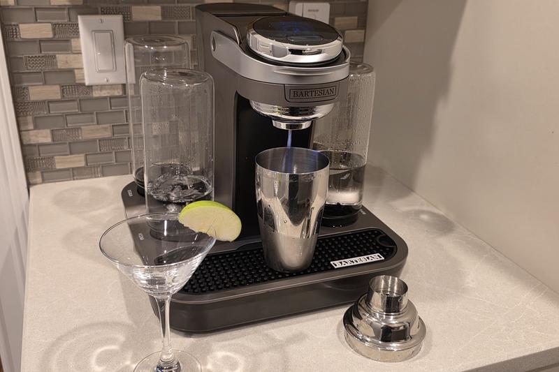 The Bartesian Premier pouring a Caramel Appletini into a stainless steel shaker, with a martini glass and a green apple slice beside it