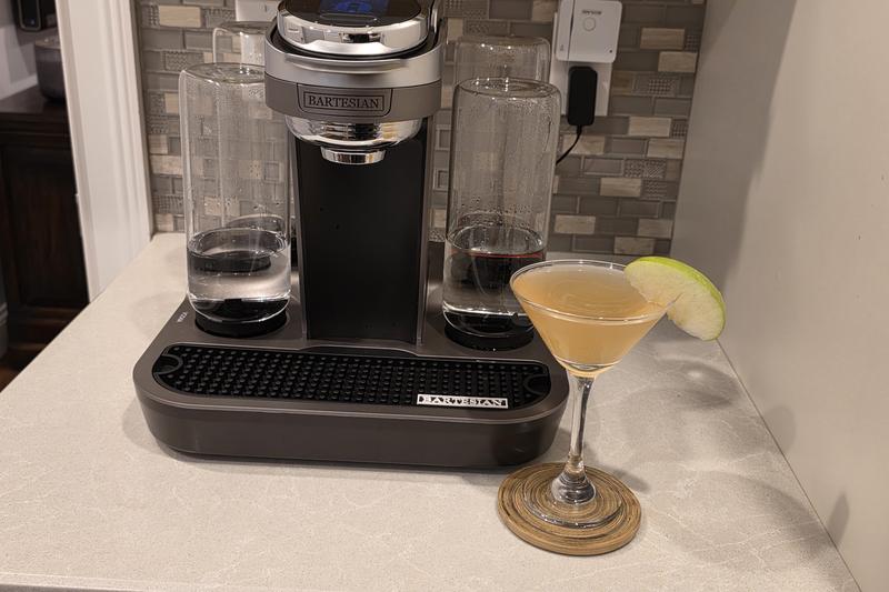A Caramel Appletini in a martini glass on a wooden coaster beside a Bartesian Premier