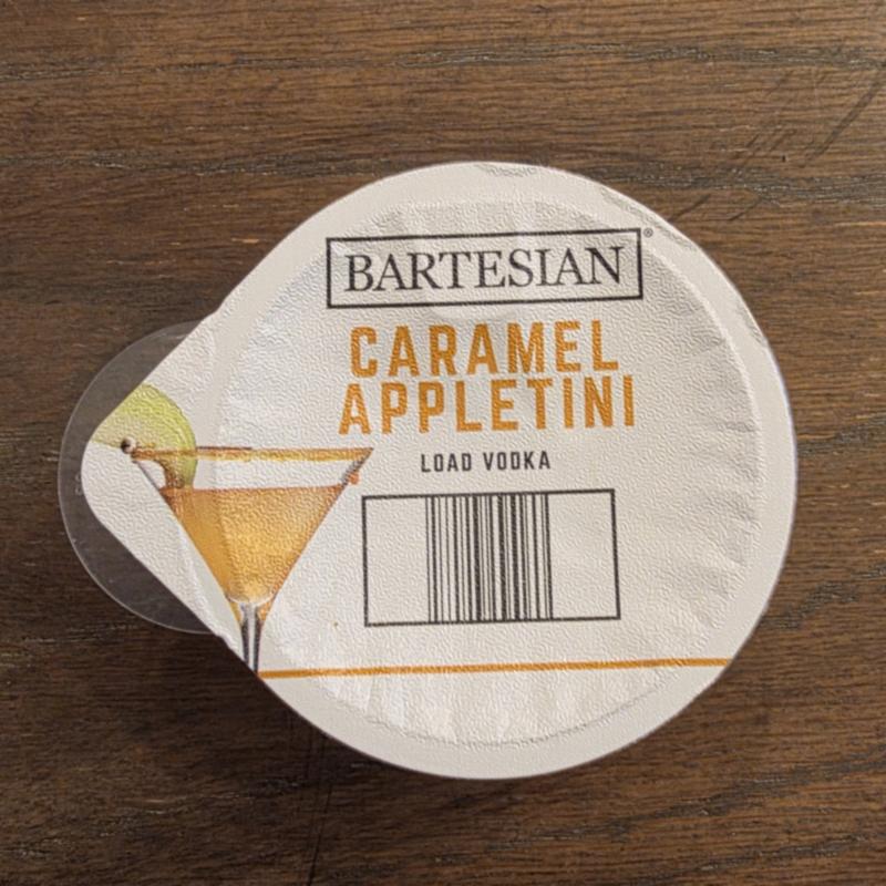 The Bartesian Caramel Appletini capsule lid on a wooden table, with the Load Vodka instruction and barcode visible
