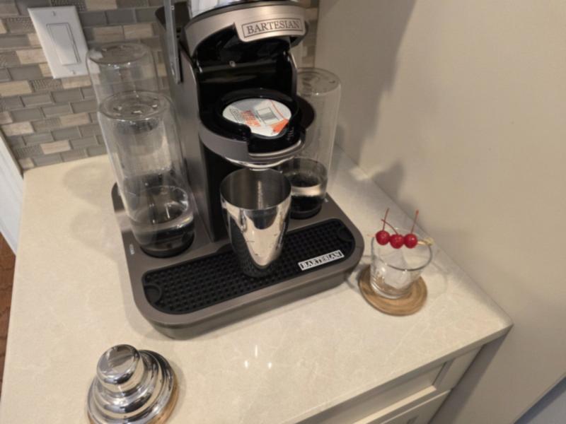 A Bartesian Premier with the Frosted Ambrosia capsule loaded and a stainless steel shaker under the spout, beside a lowball glass with cherries on a pick