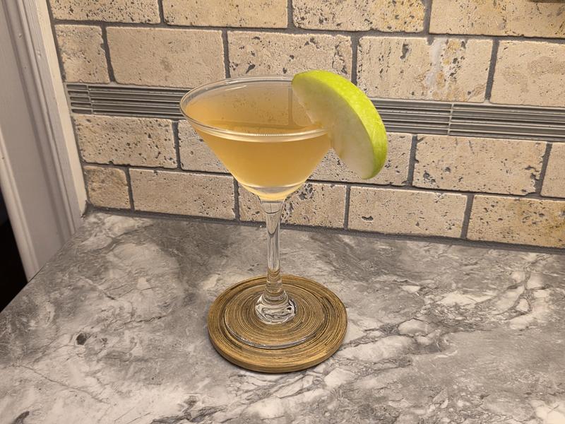 A hazy straw colored Caramel Appletini in a martini glass with a green apple slice on the rim