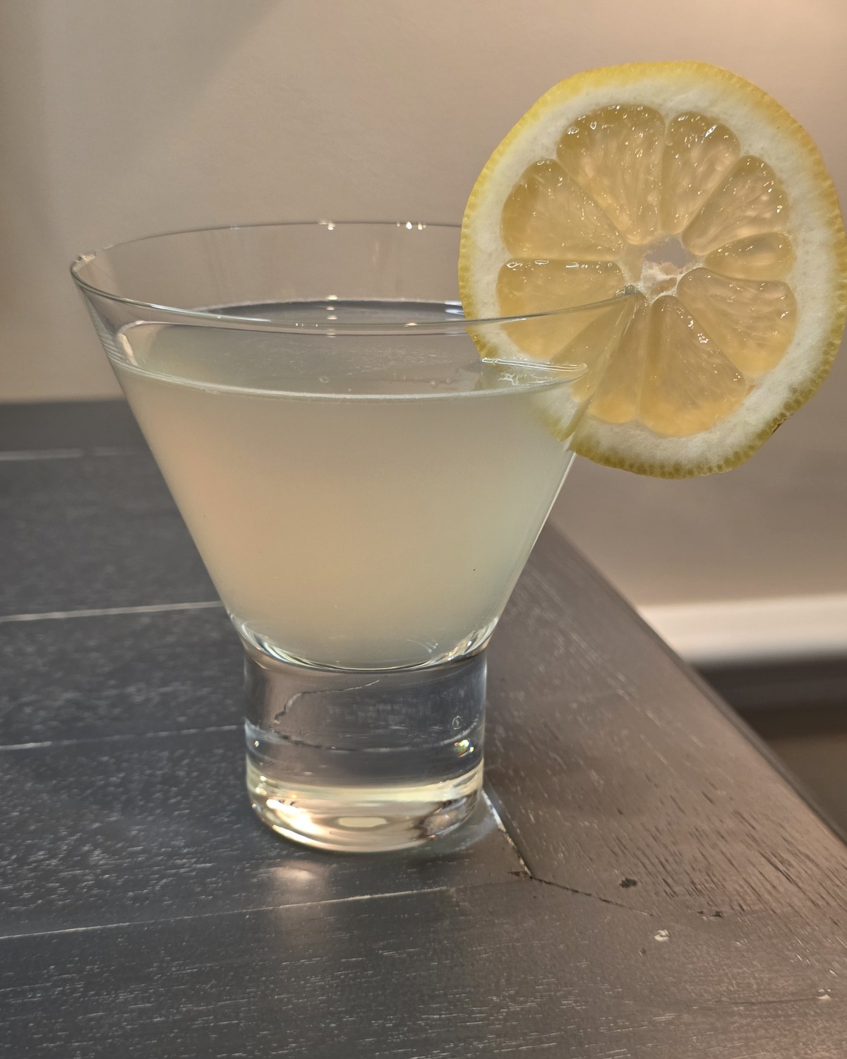 Bartesian Lemon Drop cocktail in a stemless martini glass with a hazy pale yellow color and a lemon wheel garnish on a home bar
