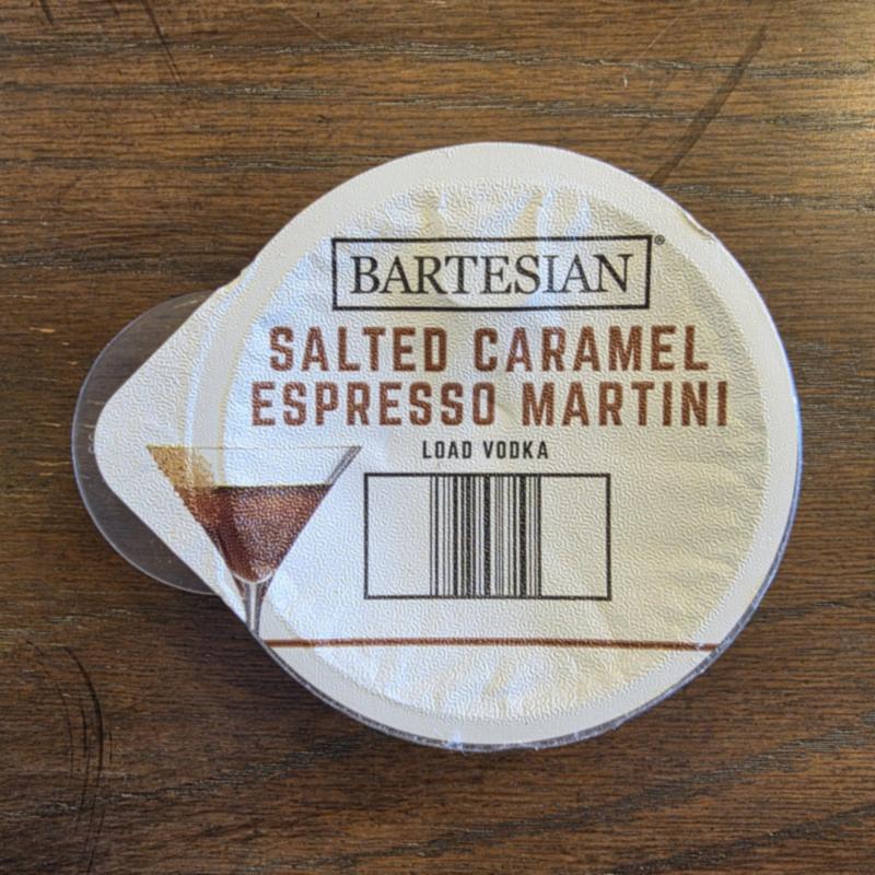 The Bartesian Salted Caramel Espresso Martini capsule lid on a dark wood table, with the Load Vodka instruction and barcode visible