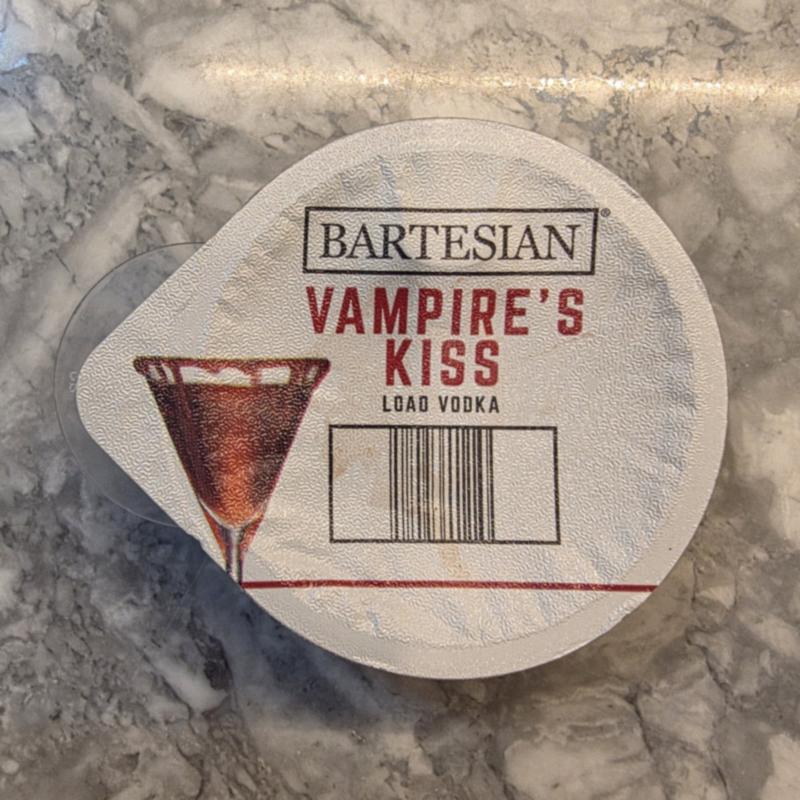 The Bartesian Vampire's Kiss capsule lid on a marble counter, with the Load Vodka instruction, a red martini glass drawing and the barcode visible