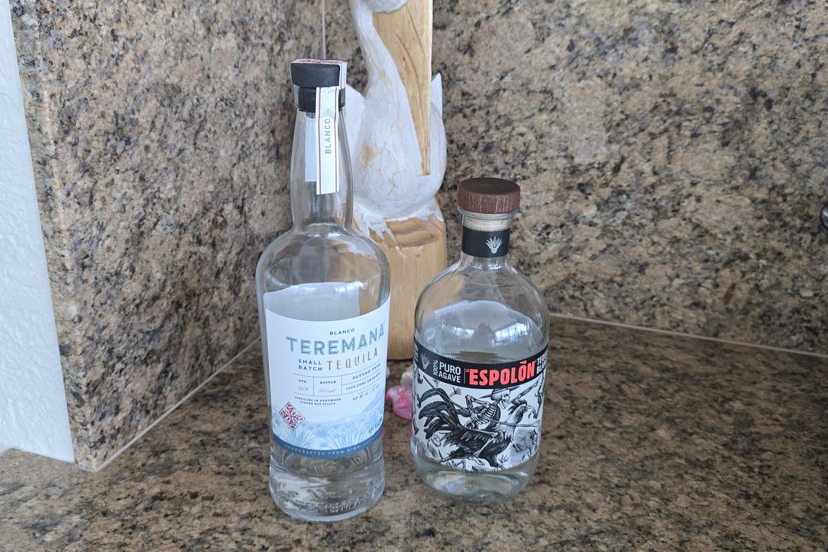 Teremana Blanco and Espolon Blanco tequila bottles side by side on a granite counter, with 100 percent puro agave readable on the Espolon label