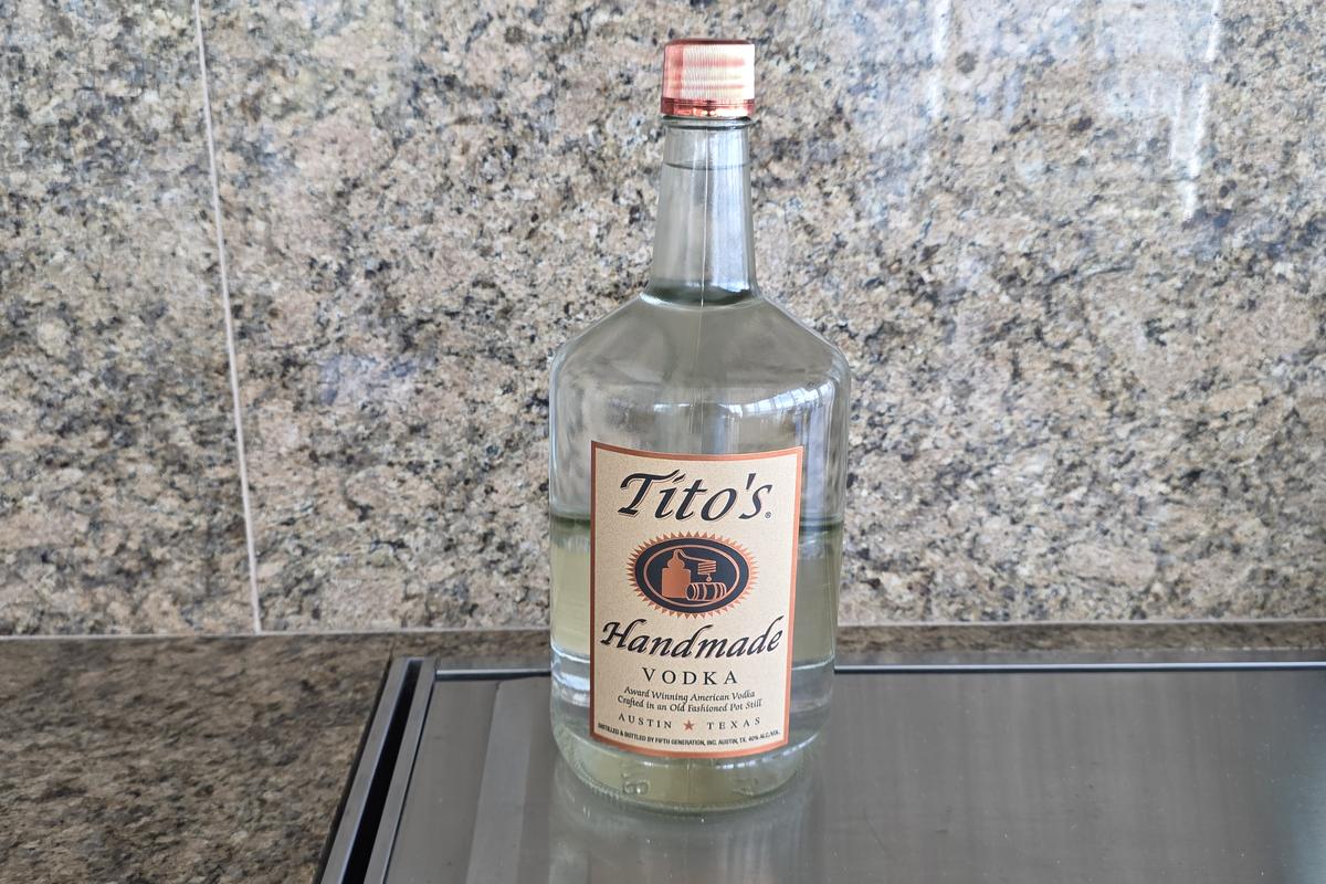 A 1.75 liter bottle of Tito's Handmade Vodka standing on a stainless counter in front of a granite backsplash