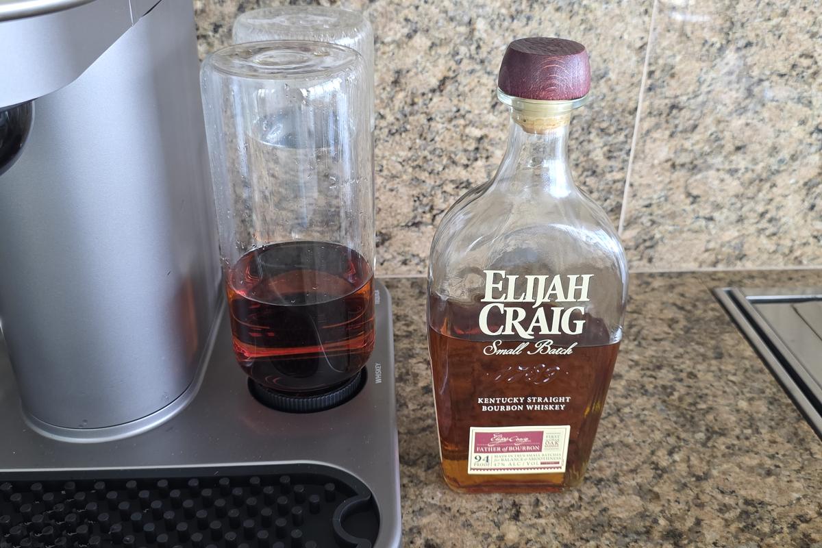 A bottle of Elijah Craig Small Batch bourbon beside the Bartesian machine, with the whiskey Spirit Bottle filled and loaded