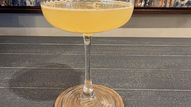 Bartesian Calamansi Daiquiri cocktail in a coupe glass with sunny yellow color and a lime garnish, on a wood coaster