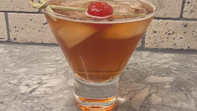 Bartesian Manhattan cocktail in a stemless martini glass over ice, garnished with a maraschino cherry, on a marble counter