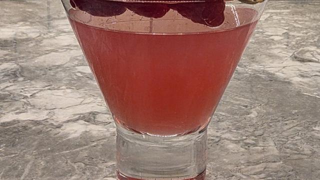 Bartesian Raspberry Ginger Gimlet cocktail in a stemless martini glass garnished with three raspberries on a marble counter