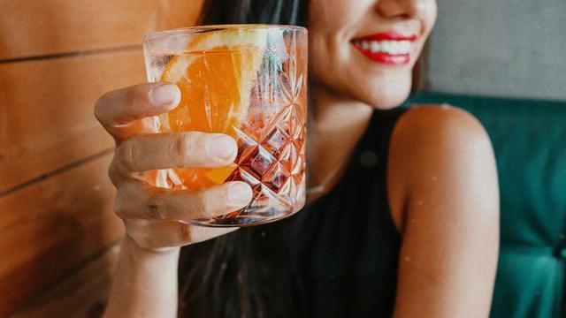 A smiling woman holding an orange cocktail in a cut crystal glass