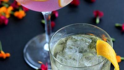 Two gin cocktails with lemon slices on a dark table scattered with flower petals