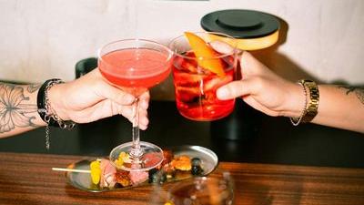 Friends toasting with colorful cocktails over a table of snacks