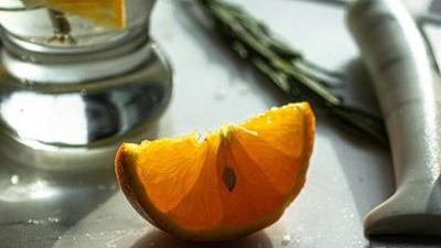 A cocktail with an orange slice and a salted rim beside a cut orange and a bar knife