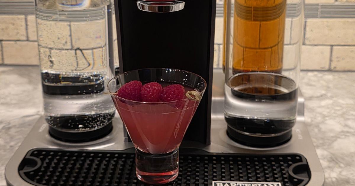 A Raspberry Ginger Gimlet with three raspberries on a pick, in a stemless martini glass on the drip tray of my Bartesian, with two Spirit Bottles behind it