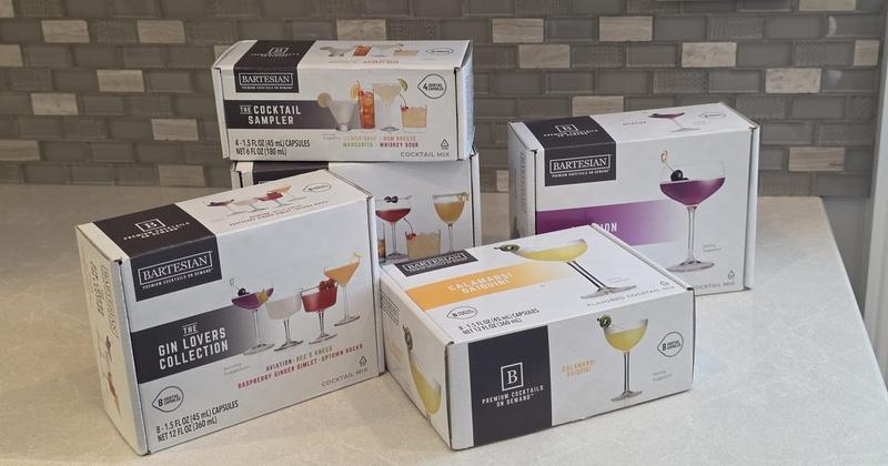 Boxes of Bartesian pods on a kitchen counter, including the Cocktail Sampler, the Gin Lovers Collection and Calamansi Daiquiri