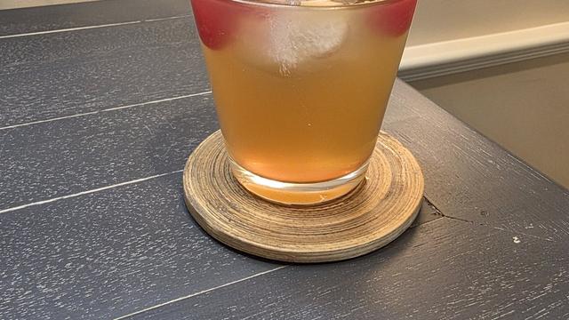 Bartesian Whiskey Sour cocktail in a low ball glass with maraschino cherries and ice on a wood coaster in a home bar corner